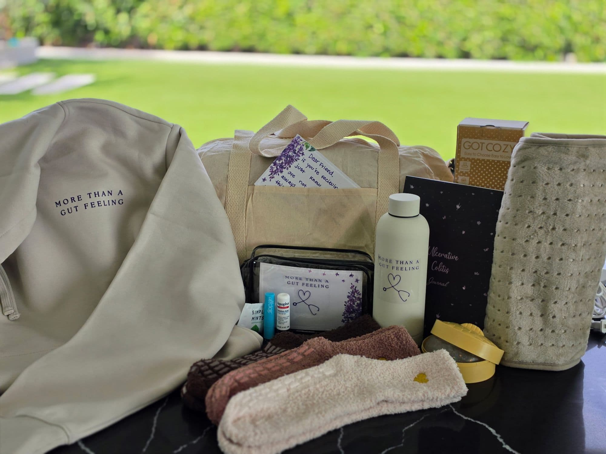 A More Than A Gut Feeling care kit, including a hoodie, journal, water bottle, socks, a heating pad, and a handwritten card